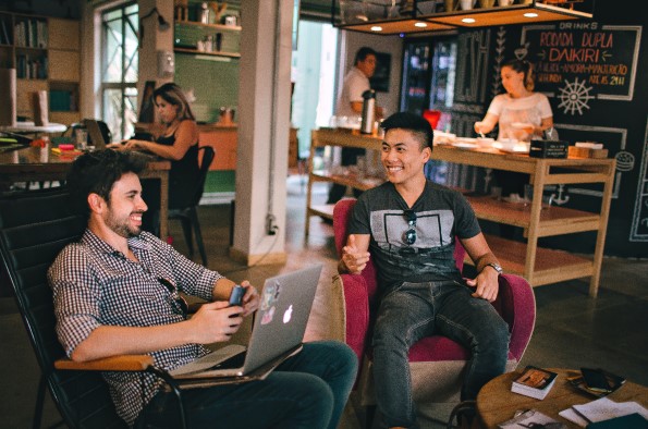 Man with laptop chatting to another man while sat in coffee shop